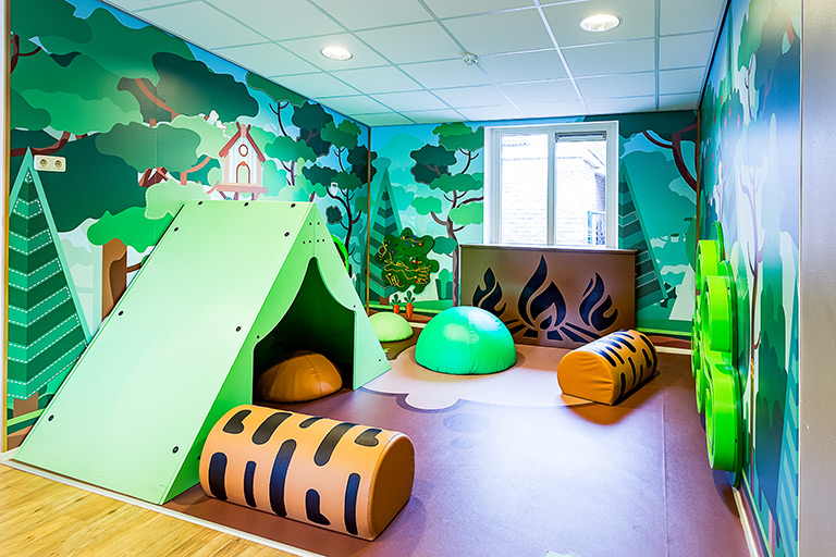 Inrichting kinderdagverblijf met een camping thema met wandspellen en softplay kussens en een tent